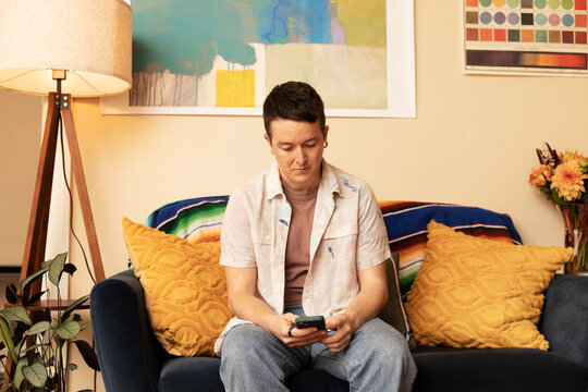 nonbinary person looking down at phone texting in apartment