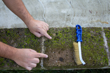 Image of the hands of a handyman using a steel brush to remove mold and moisture from bricks....