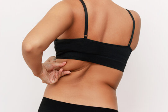 Cropped shot of a young tanned woman with waist flabs holding fat folds on her back isolated on a white background. Overweight, flabby and sagging muscles. The girl  squeezing excessive fat
