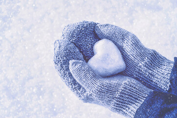 Female hands in knitted mittens with heart of snow in winter day, toned. Love concept. Valentine day background.