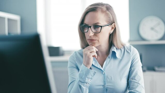 Focused mature office worker typing on computer, cheerful blonde lady in eyeglasses working in office