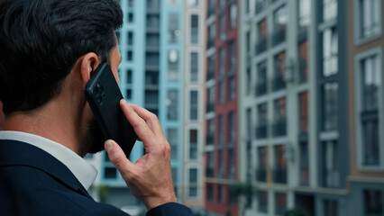 Rear back view businessman talk mobile phone outside on city street use wireless cell connection...