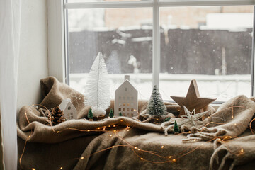 Winter hygge. Stylish christmas tree, lights, little house and wooden star on cozy blanket on...