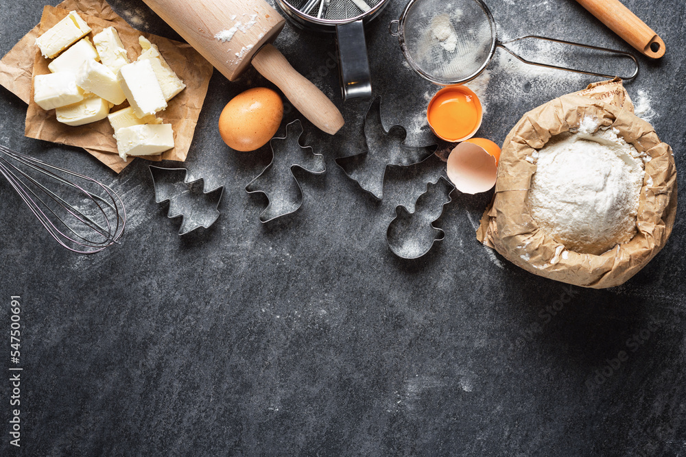 Poster ingredients for cooking baking dough with various metal shape for christmas cookies on dark backgrou