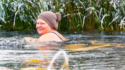 An elderly woman with knitted hat swims in the cool water of a snowy garden pond. Hardening is her lifestyle. Winter adventure is for any age.