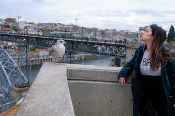 Young woman interacting with a seagull or seabird Douro river and Dom Luis I Bridge and city of Porto on background