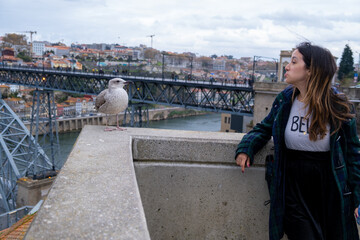 Young woman interacting with a seagull or seabird Douro river and Dom Luis I Bridge and city of Porto on background