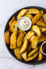Oven roasted potatoes with skins, sliced, with sauces close-up, top view