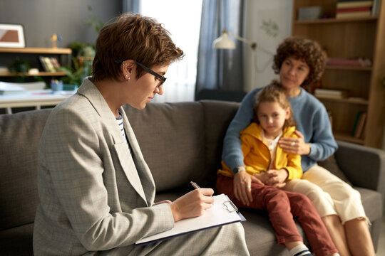 Social worker making notes in document while talking to difficult child and his mom at home