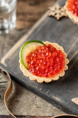 Festive New year appetizer tartlets stuffed with red caviar and a slice of lime on wooden board with vodka shots . Tasty snack for christmas or new year holiday, close up