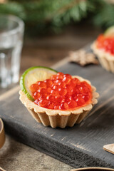 Festive New year appetizer tartlets stuffed with red caviar and a slice of lime on wooden board with vodka shots . Tasty snack for christmas or new year holiday, close up