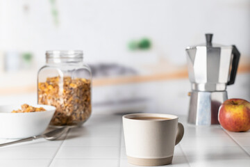 Cup of morning coffee on white tile tabletop in kitchen. Healthy breakfast consept with coffee and muesli. Text space