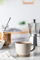 Cup of morning coffee on white tile tabletop in kitchen. Healthy breakfast consept with coffee and muesli. Text space