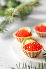 Festive Christmas appetizer tartlets stuffed with red caviar and a slice of lime on a white tray. Tasty snack for christmas or new year holiday food recipe