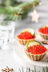 Festive Christmas appetizer tartlets stuffed with red caviar and a slice of lime on a white tray with alcohol vodka shots . Tasty snack for christmas or new year holiday, food recipe