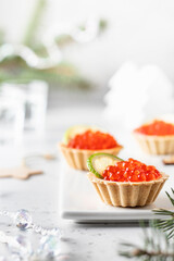 Festive Christmas appetizer tartlets stuffed with red caviar and a slice of lime on a white tray with alcohol vodka shots . Tasty snack for christmas or new year holiday, food recipe