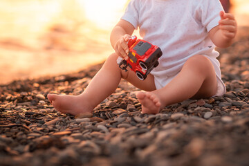 Cute little child is sitting on pebble beach and playing with toy car. Close-up. Concept of adoption of children and happy childhood