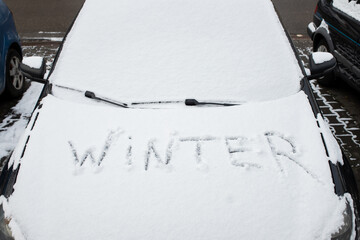 Winter written in snow on car. Winter concept. Close-up rearview mirror. The vehicle is covered...