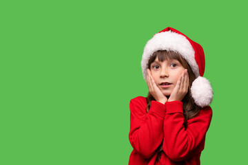 Emotional portrait. A little girl in a Santa hat holds her hands near her face in surprise. Christmas and New Year brings many surprises and dreams come true