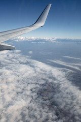 Fototapeta premium Flying above the white clouds on a beautiful landscape sky from an airplane window with the wing in the frame