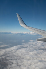 Flying above the white clouds on a beautiful landscape sky from an airplane window with the wing in the frame