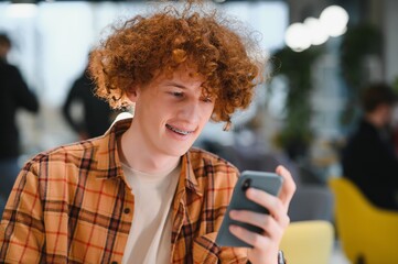 Portrait of Caucasian male freelancer in trendy apparel sitting at cafeteria table and doing remote work for programming design of public website, skilled software developer posing in coworking space.