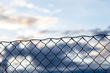 blue beautiful light sky where on one side there are dark blue gray clouds and below them you can see the dark silhouette of a metal fence