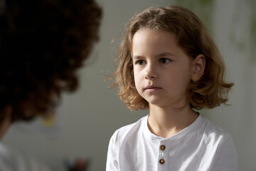 Naughty little boy listening to his mom during serious conversation at home