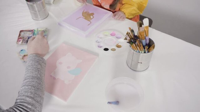 Little girl painting with acrylic paint on canvas with her mother for a distant learning art project.