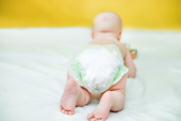 Rear view of a child crawling in a pump. Infant hygiene. Protection against the flow of urine for newborns. Child care. Cute baby on a white sheet and against a yellow wall