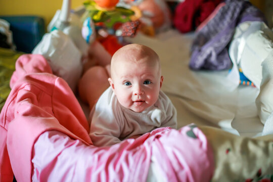 Cute little girl peeks out of the crib. The sides of the crib are hung with things and toys. A mess in the children's room. Misuse of the crib. The danger of strangulation in the nursery.