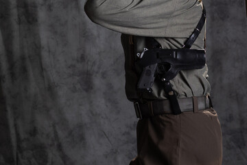 Naklejka premium A lawyer with a pistol in a holster, gray shirt and trousers with suspenders, retro style. A young man poses in the studio on a gray background. close-up of the gun