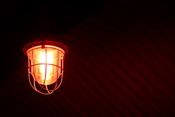 Fototapeta na wymiar An old signal lamp with red lighting hangs on the ceiling of a room, a building. The lantern creates a semi-darkness