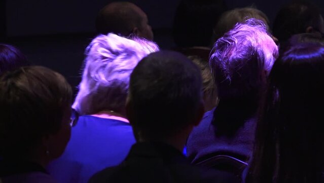 People sit with their backs in the concert hall. Human heads from behind.