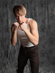 A sporty and athletic guy in a white T-shirt, boxing. A young man in a vintage outfit, posing in a studio on gray