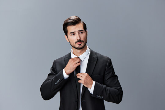 A man with a brunette beard business suit jacket white shirt and tie poses against a gray background. Business style clothing