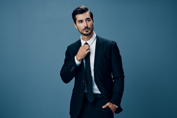 A confident business man smiles and looks at the camera in a black business suit on a blue background brunette with a beard