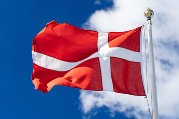 Danish flag isolated on the blue sky with clouds. Close up waving flag of Denmark.