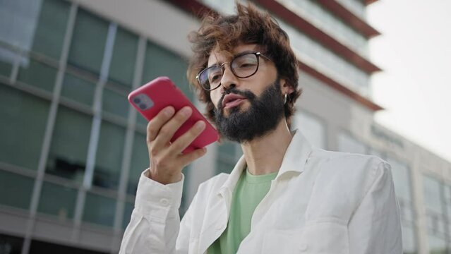 Young man with eyeglasses and beard talking on a phone call with friend in the city
