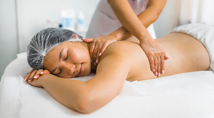 Relaxing and stress-relieving back massage. Asian woman in her 20s in a protective hair cap lying on her stomach during professional back massage procedure at her favorite SPA. High quality photo