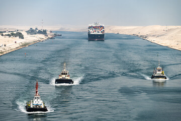 Huge cargo ships with pilot boats navigate by Suez Canal, Egypt. Concept of transportation and...