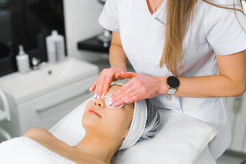 Obraz na płótnie Canvas Eye-relaxing treatment. SPA procedures concept. Caucasian long-haired unrecognizable beautician in white uniform patting the eye area of her client with cosmetic pads. High quality photo