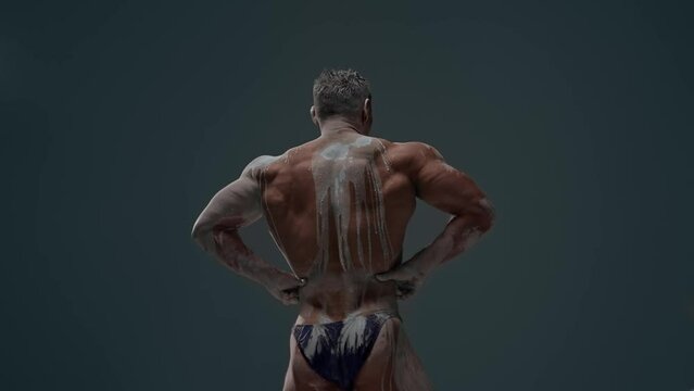 Faceless bodybuilder demonstrates inflated athletic back on white clay