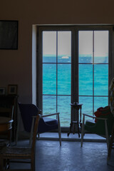 Empty tables and chairs of a restaurant by the window overlooking the sea.