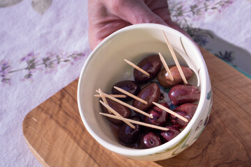 woman's hand offering Castelvetrano with wood toothpicks in a small ceramic bowl