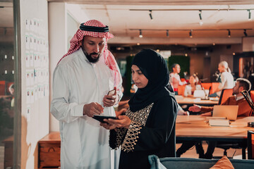 Portrait photo of Arab leader businessman with muslim hijab woman discussing business projects while using tablets and smartphone in modern glass office 