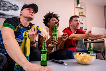 Friends watching a football match on TV, drinking beer, and cheering for their national team. World...