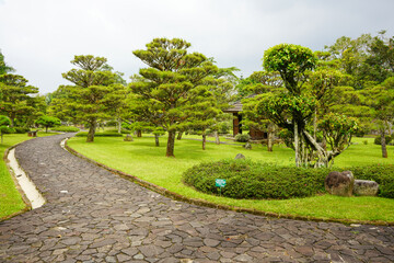 Fototapeta na wymiar A walkway in a garden made of brick traverses the edge and amidst lawn or meadow in a flower garden. Tourist, travel, holiday and vacation spot Taman Bunga Nusantara, Cianjur, Indonesia