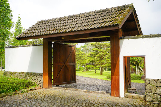 Fence and wall of oriental style houses from Japan, China or Korea. A concrete wall with a wooden gate and a tiled roof above. Rooftile gate.