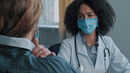 Doctor african woman caregiver in medical mask consult sick man at hospital male patient suffer from neck pain back muscle tension. Female physician listen health complaint give medical consultation - Powered by Adobe